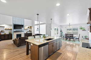 Kitchen featuring light stone countertops, a kitchen bar, open floor plan, dishwasher, and light wood-type flooring