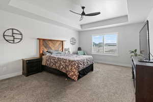 Carpeted bedroom featuring a tray ceiling and ceiling fan