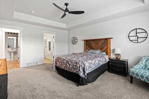 Bedroom with a tray ceiling, light colored carpet, and a ceiling fan