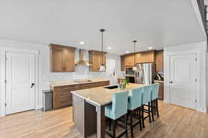Kitchen featuring a kitchen bar, a center island with sink, brown cabinetry, appliances with stainless steel finishes, and light stone countertops