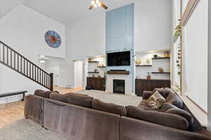 Living room with ceiling fan, stairway, a high ceiling, light wood-style floors, and a large fireplace