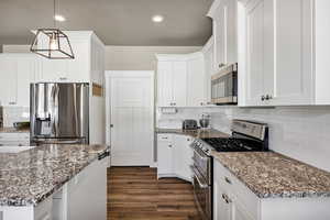 Kitchen featuring decorative backsplash, stainless steel appliances, decorative light fixtures, dark stone counters, and white cabinets
