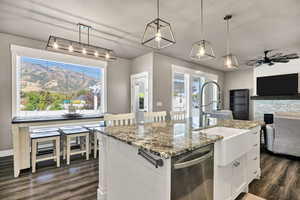 Kitchen with hanging light fixtures, light stone counters, stainless steel dishwasher, an island with sink, and a textured ceiling