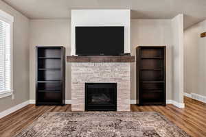 Unfurnished living room featuring wood finished floors and a stone fireplace