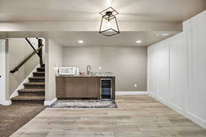 Indoor wet bar with stairs, beverage cooler, light stone counters, light wood-style floors, and recessed lighting