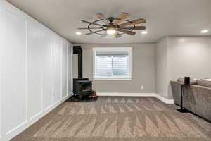 Unfurnished living room with a wood stove, carpet floors, recessed lighting, a ceiling fan, and a decorative wall