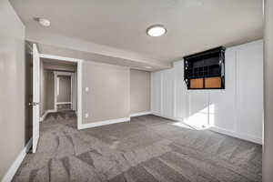 Carpeted empty room featuring a textured ceiling and a smoke detector