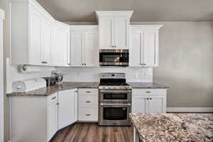 Kitchen with stainless steel appliances, white cabinetry, tasteful backsplash, and dark stone counters