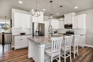 Kitchen with appliances with stainless steel finishes, hanging light fixtures, a kitchen breakfast bar, white cabinetry, and recessed lighting