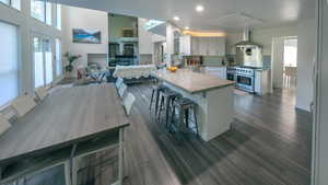 Kitchen featuring decorative backsplash, a peninsula, a kitchen bar, light countertops, and wall chimney exhaust hood