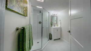 Full bath featuring vanity, a textured ceiling, a shower stall, and light tile patterned floors
