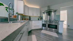 Kitchen with double oven range, wall chimney range hood, tasteful backsplash, dark wood-style floors, and white cabinetry