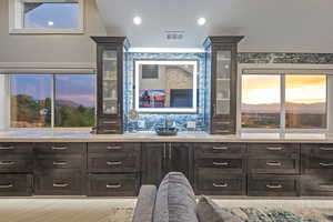 Bar area featuring dark brown cabinets, decorative backsplash, healthy amount of natural light, glass insert cabinets, and recessed lighting