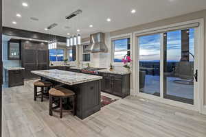 Kitchen featuring a kitchen breakfast bar, island exhaust hood, decorative light fixtures, dark brown cabinetry, and recessed lighting
