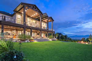 Rear view of house featuring a mountain view, a yard, a fire pit, a ceiling fan, and a balcony