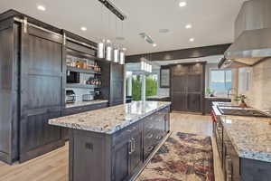 Kitchen featuring dark brown cabinetry, light wood-style flooring, ventilation hood, light stone counters, and recessed lighting
