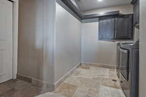 Laundry room featuring stone tile floors, a textured ceiling, separate washer and dryer, and cabinet space