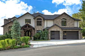 Craftsman-style home featuring board and batten siding, a garage, stone siding, and driveway