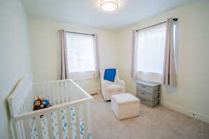 Carpeted bedroom featuring baseboards and a nursery area