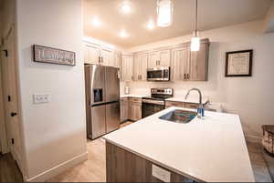 Kitchen featuring appliances with stainless steel finishes, light wood-type flooring, light stone counters, hanging light fixtures, and recessed lighting