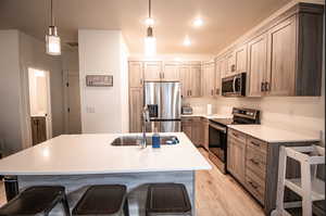 Kitchen featuring stainless steel appliances, a breakfast bar, pendant lighting, light wood-style flooring, and light stone counters