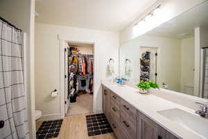 Full bath featuring double vanity, light wood-style flooring, a spacious closet, and a shower with curtain
