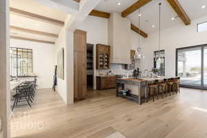 Kitchen featuring a kitchen bar, a large island with sink, pendant lighting, backsplash, and light wood-type flooring
