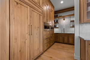 Kitchen featuring brown cabinets, decorative backsplash, light wood-type flooring, and open shelves