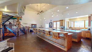 Kitchen featuring a ceiling fan, high vaulted ceiling, a textured ceiling, open floor plan, and a breakfast bar area