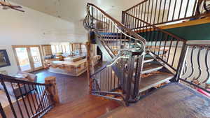 Staircase with high vaulted ceiling, hardwood / wood-style flooring, and ceiling fan