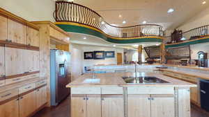 Kitchen with light brown cabinetry, stainless steel refrigerator with ice dispenser, dark wood-style flooring, recessed lighting, and a towering ceiling