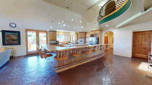 Kitchen featuring arched walkways, a kitchen bar, stainless steel fridge with ice dispenser, a high ceiling, and light brown cabinetry