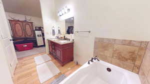 Full bath featuring a garden tub, vanity, and light wood finished floors
