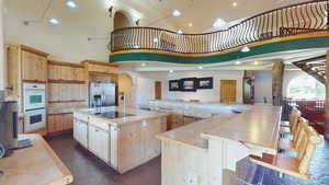 Kitchen with light brown cabinetry, light countertops, stainless steel refrigerator with ice dispenser, white double oven, and a towering ceiling