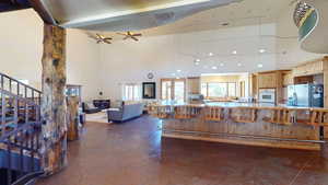 Kitchen featuring a kitchen bar, a towering ceiling, a ceiling fan, stainless steel refrigerator with ice dispenser, and open floor plan