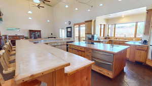 Kitchen featuring a breakfast bar area, hanging light fixtures, a ceiling fan, a warming drawer, and a towering ceiling