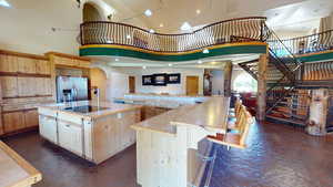 Kitchen featuring light brown cabinets, stainless steel fridge with ice dispenser, a kitchen breakfast bar, a towering ceiling, and black electric cooktop