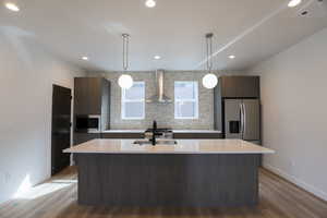 Kitchen featuring modern cabinets, wall chimney exhaust hood, light wood-type flooring, an island with sink, and recessed lighting