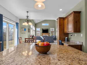 Kitchen featuring open floor plan, light stone countertops, a chandelier, vaulted ceiling, and brown cabinetry