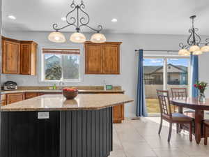 Kitchen featuring brown cabinets, light stone counters, pendant lighting, a chandelier, and recessed lighting