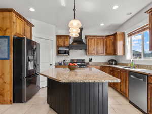 Kitchen featuring stainless steel appliances, light stone countertops, hanging light fixtures, light tile patterned flooring, and wall chimney range hood