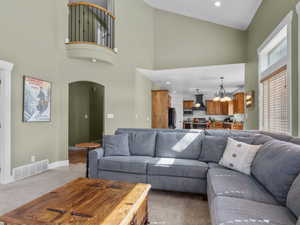 Living area featuring high vaulted ceiling, arched walkways, light colored carpet, and recessed lighting