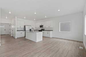 Open-concept living space featuring wood-finish flooring, recessed lighting, and a kitchen with white cabinetry