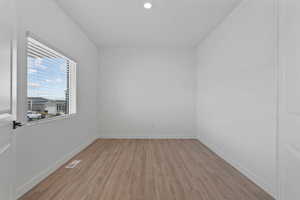 Bright room featuring wood-finish flooring, white baseboards, a single window with horizontal blinds, and a recessed ceiling light