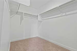 Walk-in closet featuring white wire shelving, metal hanging rods, light-colored carpet, white walls, and white baseboards