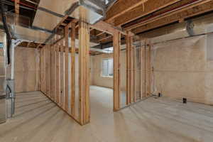 Unfinished basement space featuring exposed wood framing, concrete flooring, insulated walls, an egress window, and visible ductwork