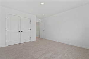 Neutral tone wall finish, plush carpet flooring, recessed ceiling light, white baseboards, and double closet doors with dark hardware