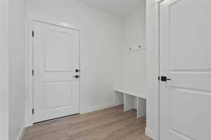 Entryway featuring light wood-finish flooring, white walls, and a built-in bench with storage cubbies and coat hooks