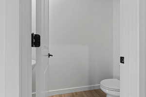 Powder room with wood-finish flooring, white walls, and a white toilet