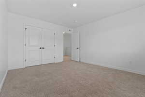 Neutral toned carpet flooring, white walls, white baseboards, and recessed lighting